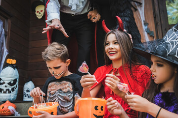 happy kids in halloween costumes holding buckets with lollipops near parents