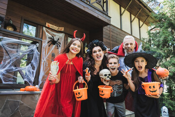 Naklejka premium cheerful family in spooky halloween costumes grimacing at camera near house