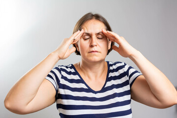 Woman having headache on grey background. Exhausted girl portrait. Female wearing casual clothes feeling fatigue and headache. stress and frustration concept.