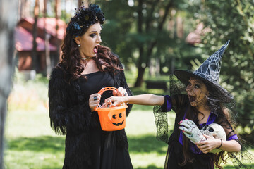 excited woman in vampire halloween costume screaming while daughter stealing candies from bucket