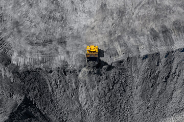 Loading coal, yellow truck handling anthracite in open mine, aerial top view