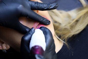 the master holds a tattoo machine and performs permanent makeup stretching the lips of the model
