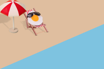 Creative funny composition made of sun umbrella, fried egg with sunglasses sitting on deck chair on...