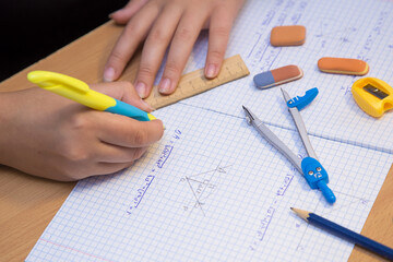 Pupil's hand in close-up solve a geometry problem in a notebook. A schoolboy performs a task at the workplace. The concept of children's education, teaching knowledge, skills and abilities.