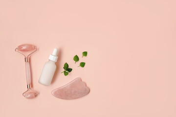 Composition of white mockup serum bottle, pink quarts stone face roller and gua sha stone with fresh leaves on pink background. Natural cosmetics concept. Creative cosmetics flat lay with copy space.