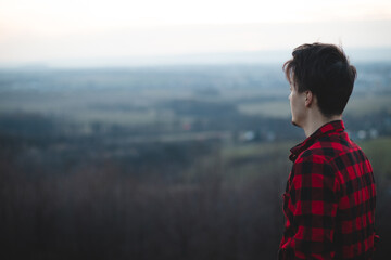 Candid portrait of a man in his 20s dressed in a black and red checked shirt looking into his future, immersed in his thoughts and contemplating. Authentic mood of a young man on an indecisive journey