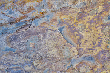 Rough stone texture with rust in blue and yellow colors with orange placed on a wall on a facade
