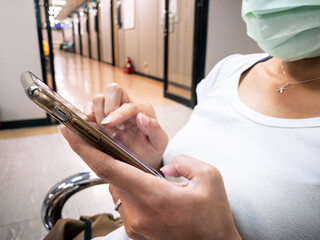 Asian woman using smartphone and wearing a surgical mask in a hospital.