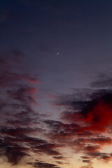 Colorful cloudy sunset sky with small crescent moon high in frame