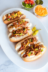 Close up of plate of chili dogs and toppings on white marble counter.