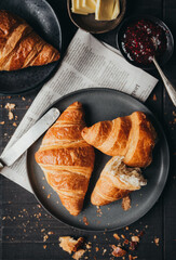 Close up of plates of croissants with jam and butter on black table.