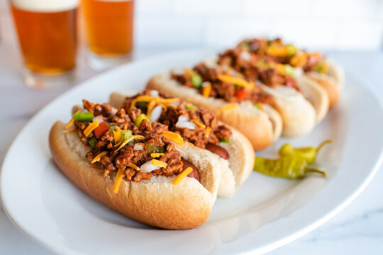Close up of a plate of chili dogs with glasses of beer in background.