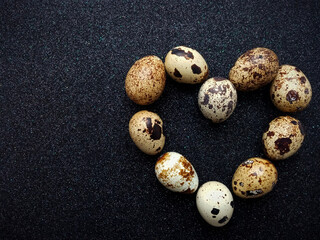tten quail eggs in the shape of a heart on a black background closeup - obrazy, fototapety, plakaty