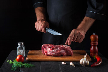 The chef cuts meat with a knife in the kitchen prepares food. Vegetables and spices on the kitchen table in a restaurant to prepare a delicious lunch