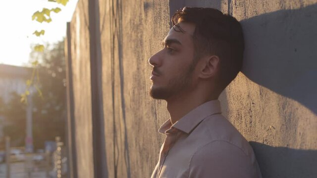 Side view portrait hispanic business man male serious pensive dreamy face young bearded boss leader businessman tourist guy stands alone in city leaning against stone wall outdoors dreaming thinking