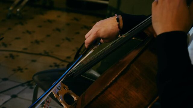 Artist plays with a bow on the strings of the cello in the darkness. Close-up musician plays with a bow of a violoncello
