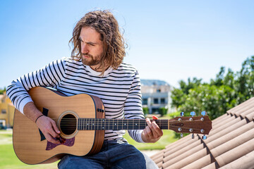 Attractive man with long hair playing acoustic guitar outdoors