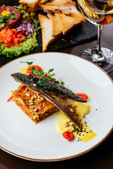 grilled fish in a plate with vegetables and sauce