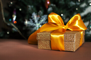 Shiny gift box with a large golden ribbon bow on a blurred background. A beautiful gift for the new year, christmas. Soft focus. Copy space.
