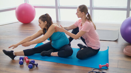 Fototapeta na wymiar Pregnant Woman Goes in for Sports in the Gym. Personal Fitness Trainer Helps you with Exercise for Pregnant Women. Preparing the Body for Childbirth. Pregnancy, Sport and Health Concept.
