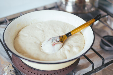 Yeast dough and wooden spoon in enameled bowl on stove