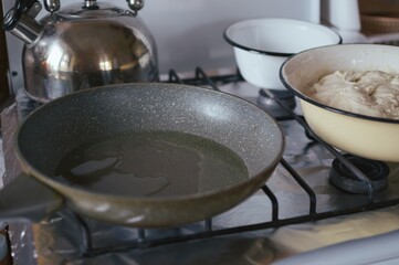 Frying pan with oil heated on stove. Bowl of dough and other utensils.
