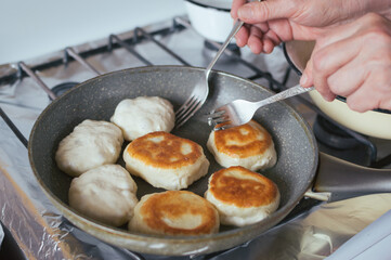 Women's hands turn over donuts in frying pan with forks