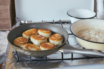 Yeast pancakes are fried in a frying pan on stove. Dough in bowl