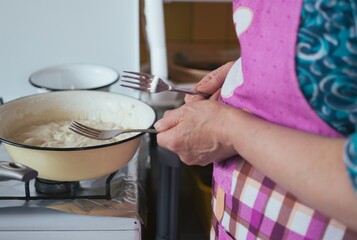 Middle-aged woman cooking with forks in hands. Bowl of dough on stove