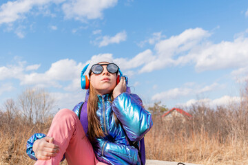 Teenage girl in mirrored sunglasses looks into the sky. Wellness concept. Child listens to music and sings