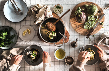 Hands of people eating stuffed Artichokes at dinner table