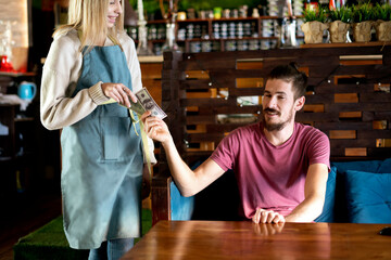young man paying waitress for his order in restaurant
