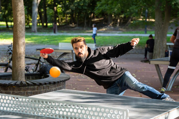 Playing table tennis outdoors on the open air sport ground. Charismatic man in with beard plays...