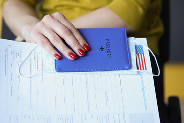 Female hand holding passport with protective medical face mask and document for obtaining American...