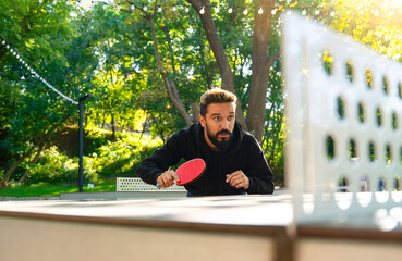 Street table tennis on the open air ground. Game focused man plays ping pong. - obrazy, fototapety, plakaty