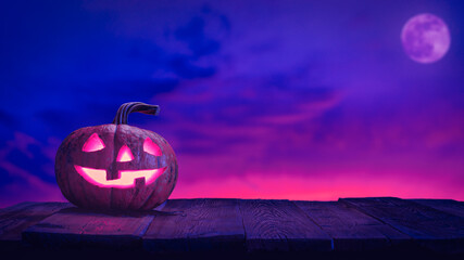 Halloween pumpkin jack o lantern on wood planks against pink and blue sky with moon