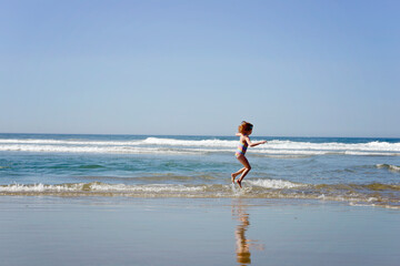 Fototapeta na wymiar Happy little redhead girl running along the ocean shore.