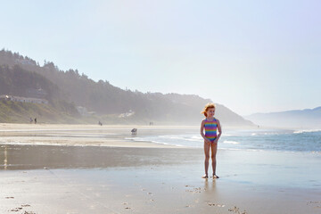 Happy little redhead girl standing on the ocean shore.