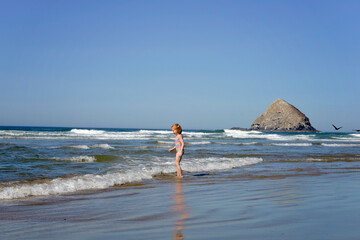 Happy little redhead girl standing on the ocean shore.