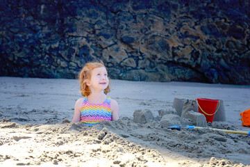Little girl buried in the sand at the beach.