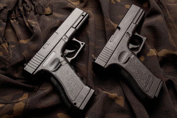 Two black pistols are lying parallel on a camouflage soldier's jacket. A firearm that makes you...