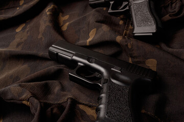 Two black pistols are lying on a camouflage soldier's jacket. A firearm that makes you think about self-defense. World Arms Day. Side view