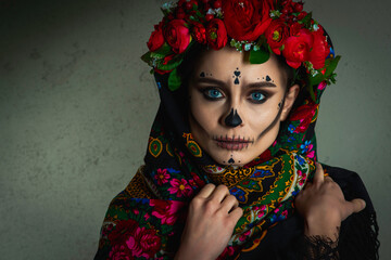 Dead gir with sugar skull makeup with a wreath of flowers on her head and skull, wearth lace gloves and showing victory sign isolated on red background.Concept of Halloween or La Calavera Catrina.