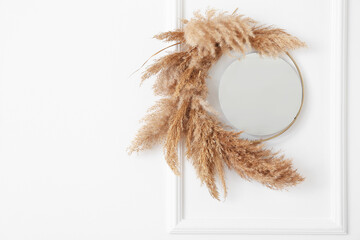 Mirror and reed branches hanging on light wall