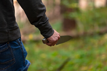 Fototapeta na wymiar A man with a large knife in the forest, close-up, selective focus. Concept: attack on passers-by, rapist and murderer, crime in the forest belt, criminal and horror.