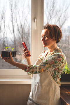 A girl takes pictures on a smartphone of plants, for her blog, which she has grown in her home garden