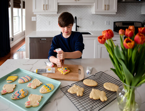 Young boy decorating Easter cookies on counter of a modern kitchen.
