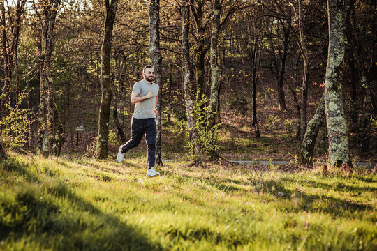 Man in cap and dark tracksuit running through the forest