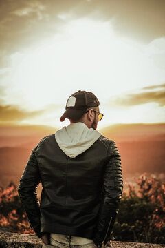 Modern guy wearing sunglasses cap and black windbreaker at sunset