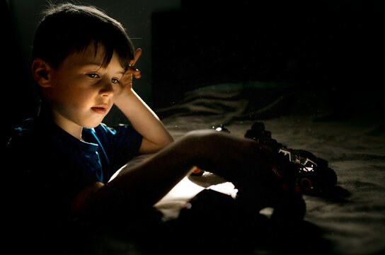 Young boy in blue shirt playing with cars on a bed in bedroom